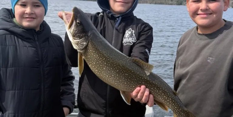 Three kids hold a fish and smile at the camera
