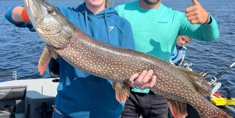 Two people holding a giant pike while giving thumbs up.
