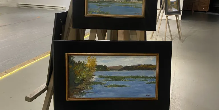 Framed landscape paintings on easels. 