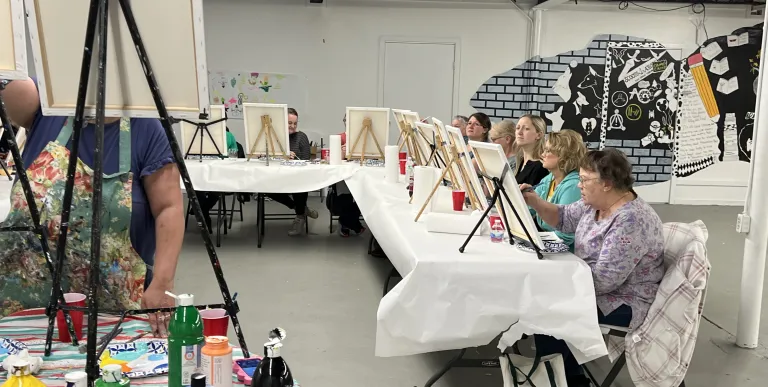 People at a long table painting on canvases.