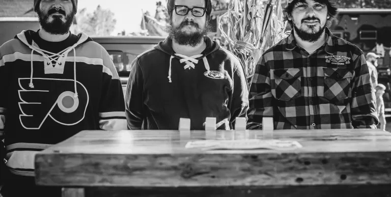 Three men display Raquette River Brewing merch