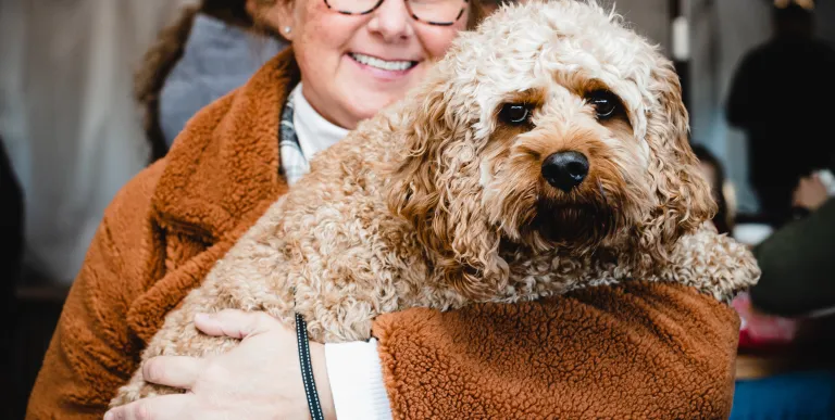 A smiling lady holds her medium sized blonde dog in this pet friendly establishment.