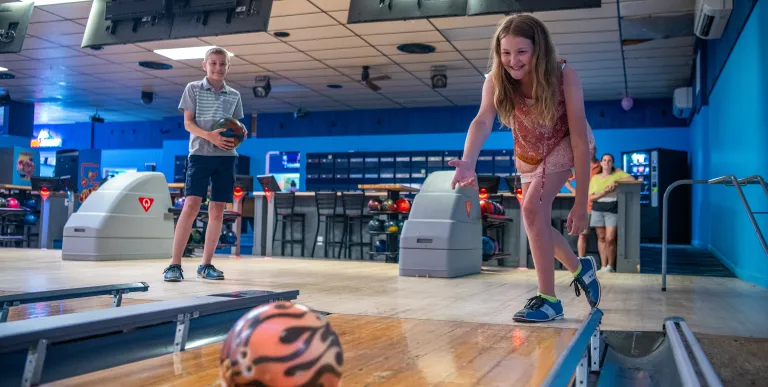 A girl throws a bowling ball with flame decor down the lane.