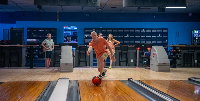 A man sends a bowling ball down the polished lane.
