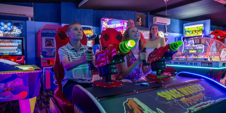 Kids play an arcade game surrounded by black light colors.