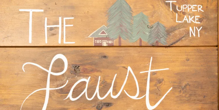 A wooden sign with white lettering The Faust Motel Tupper Lake NY