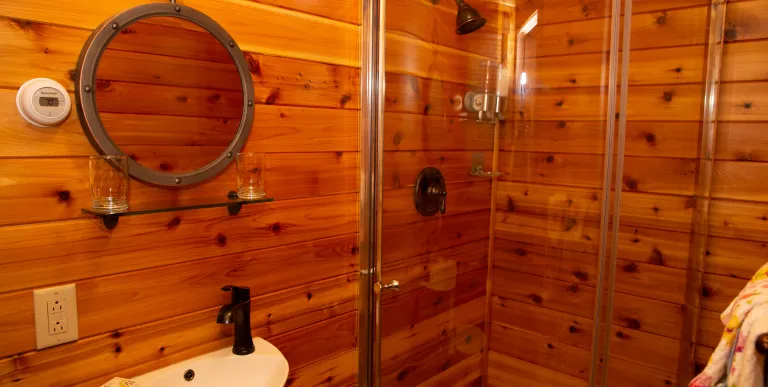 The horizontal wood paneling in the bathroom with small white sink and large curved clear shower.