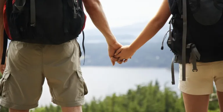Two people hold hands while looking out over pine trees and a lake