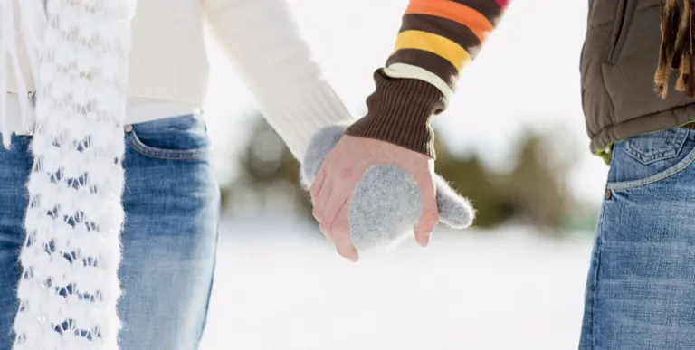 Two people holding gloved hands and walking in the snow