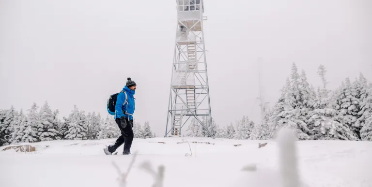 A man walks in front of a firetower in the winter