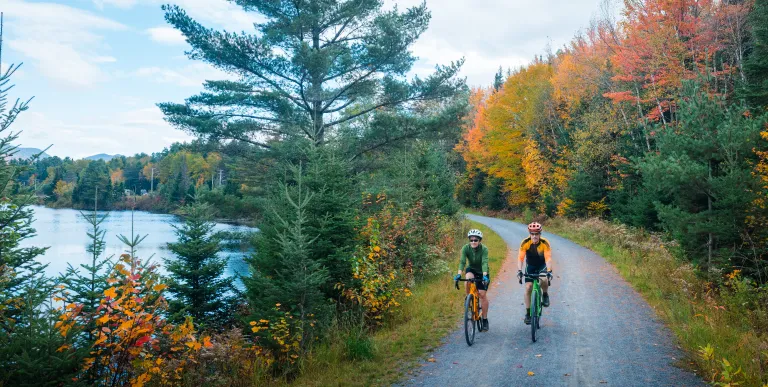 Two cyclists ride on a smooth gravel trail in fall