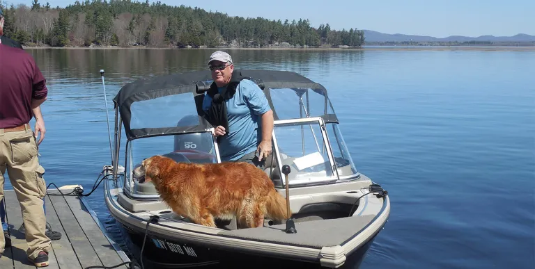 A boat tied at a launch with a man and golden retriever