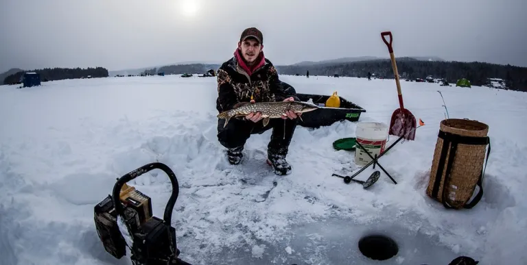 A guy holding up a fish during the winter