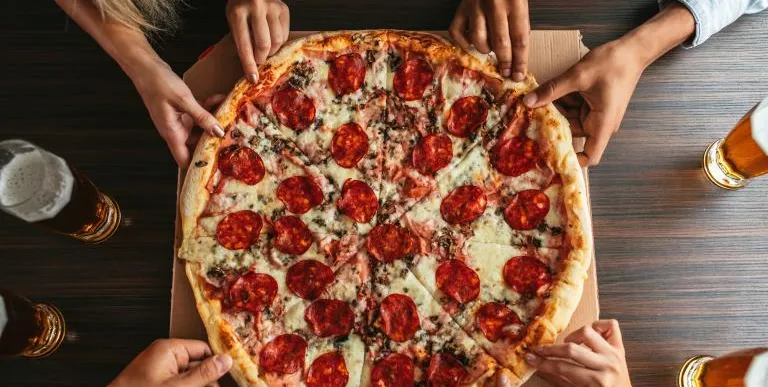 Lots of hands reach to pull a slice of pizza