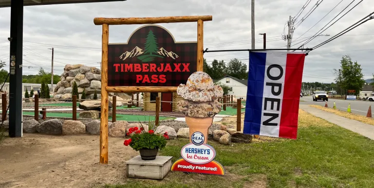Timberjaxx Pass Ice Cream and Mini Golf shop Tupper Lake Sign with open flag.