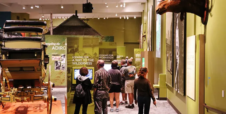 A large room with green walls and high ceilings where people are viewing the plaques under various displays like a carriage and a moose.
