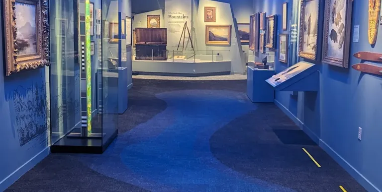 Art pieces on display in a long hallway with blue walls