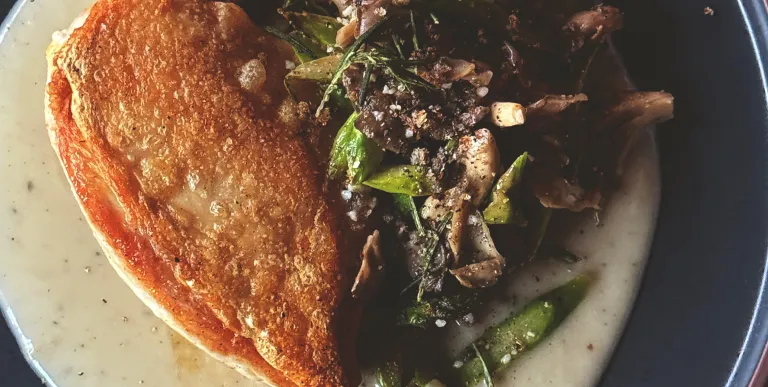 A pan fried chicken thigh with mushroom side dish over cream base.