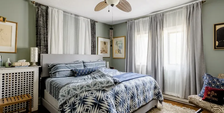 A guest bedroom with large bed floor to ceiling window treatments and light accents.