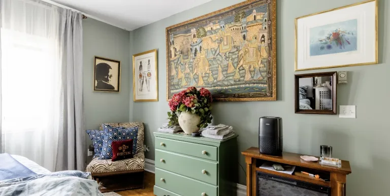 A guest bedroom with electric fireplace and wingback chair.