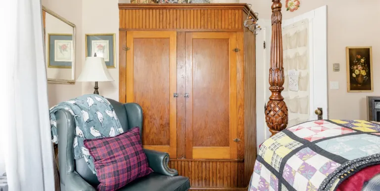 large wooden wardrobe with a leather wingback chair in a guest room