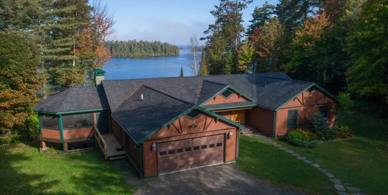 An aerial view of a cabin by a lake surrounded by tall pines.
