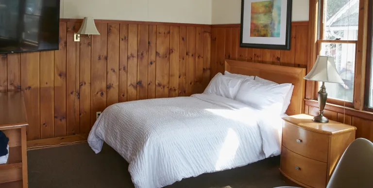 Plush white linens on a queen bed in a wood paneled room at The Ashley.