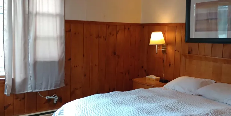 Plush white linens on a queen bed in a wood paneled room at The Ashley.